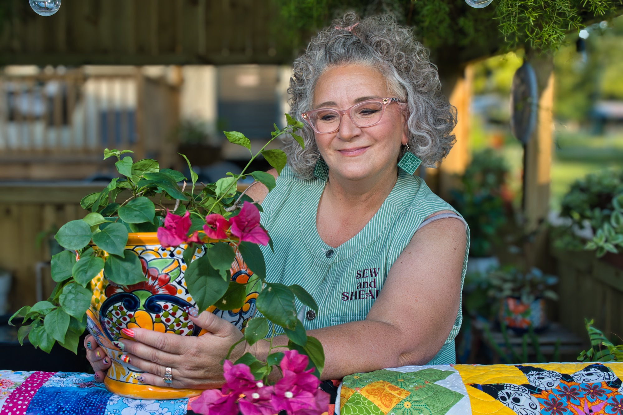 Angela in her garden pergola holding a pot of pink bougainvillea over a patchwork quilt