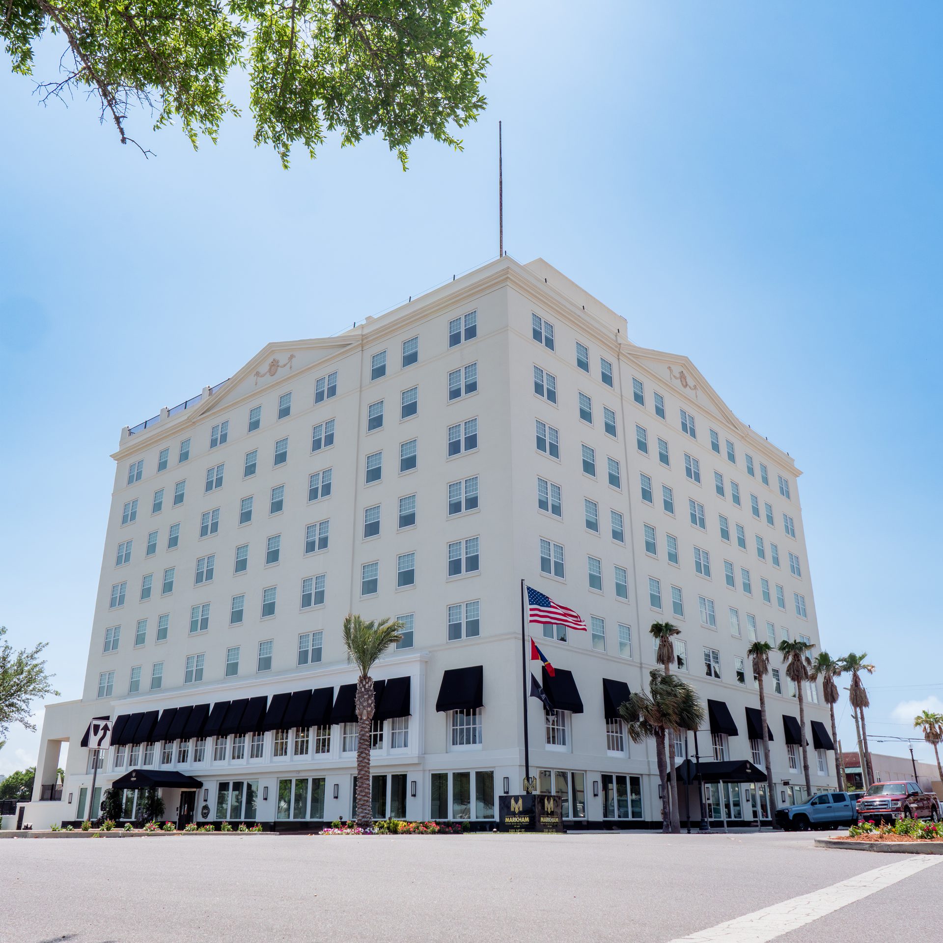 The Markham Hotel, a white historic high-rise with black awnings and palms, seen from the street corner in downtown Gulfport