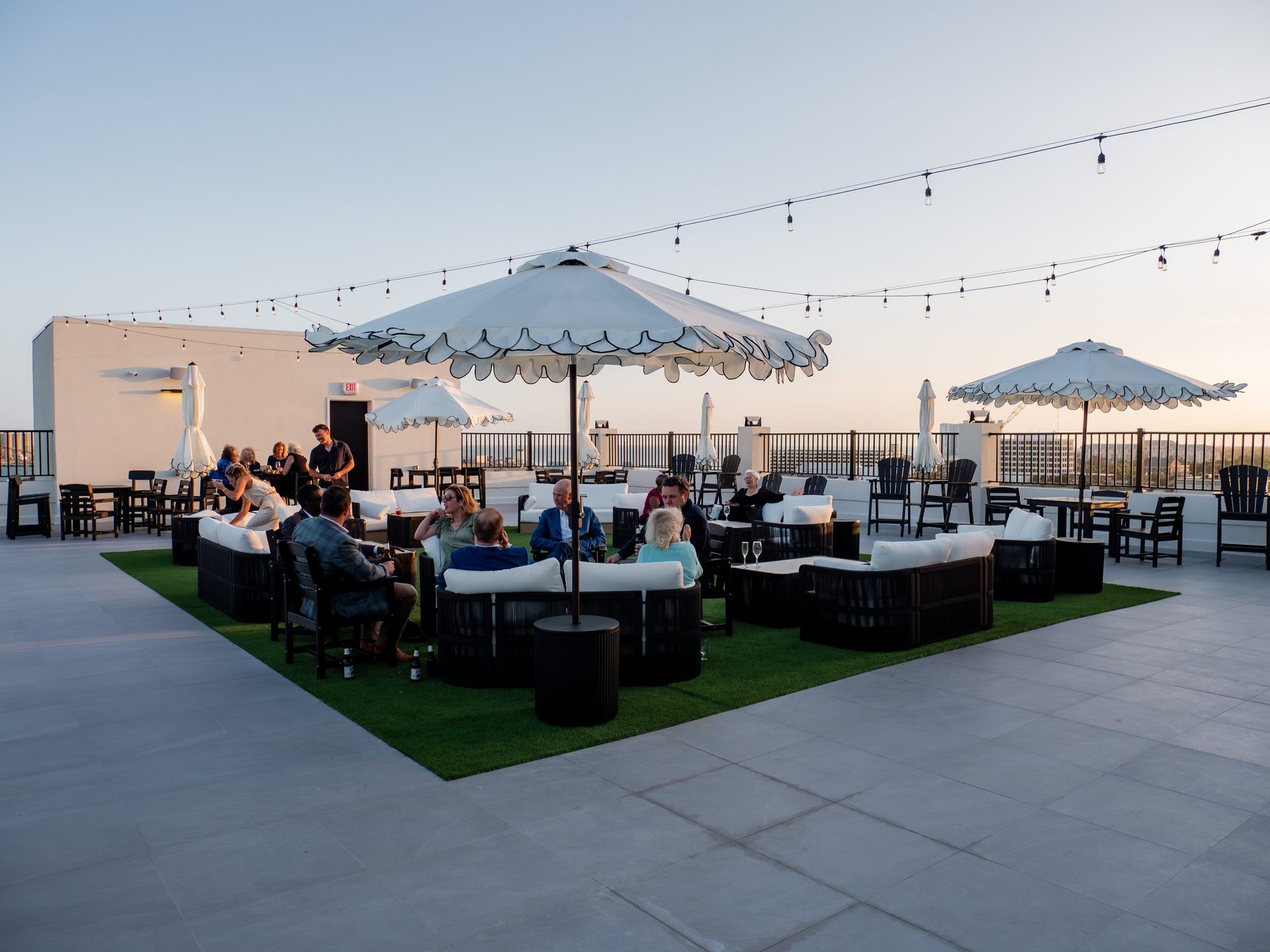 The rooftop terrace of the Markham Hotel at dusk, with guests seated under white scalloped umbrellas and string lights